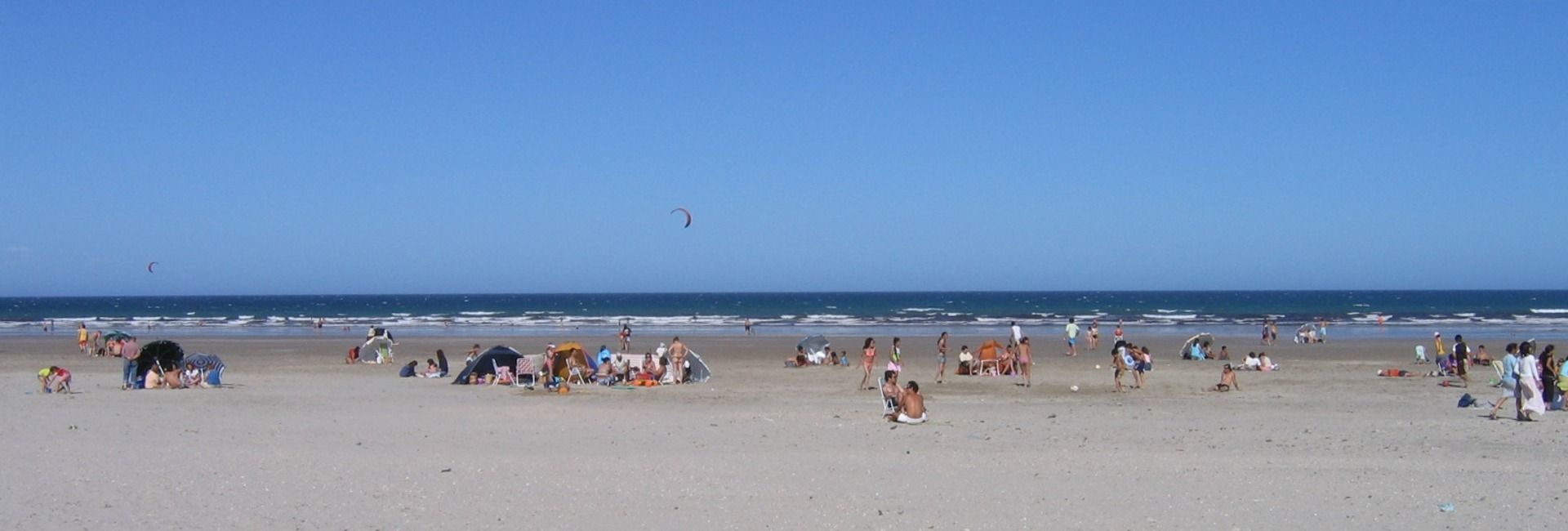 Beach scene with people on the sand, blue sky and ocean in the background.