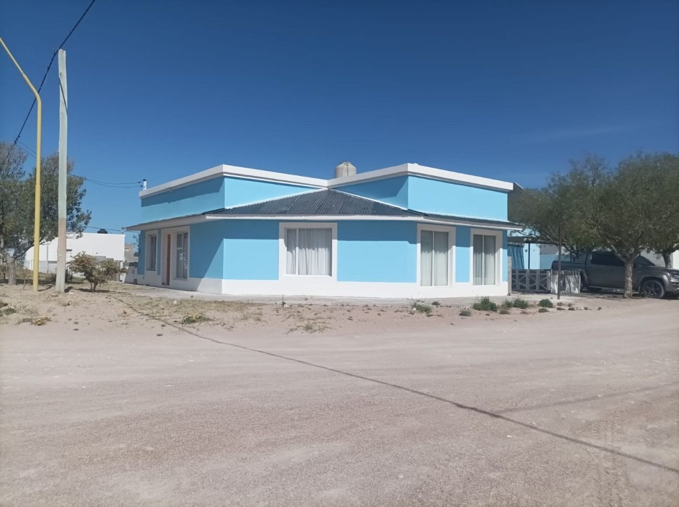 Light blue building with white trim under a clear blue sky, on a dirt road.