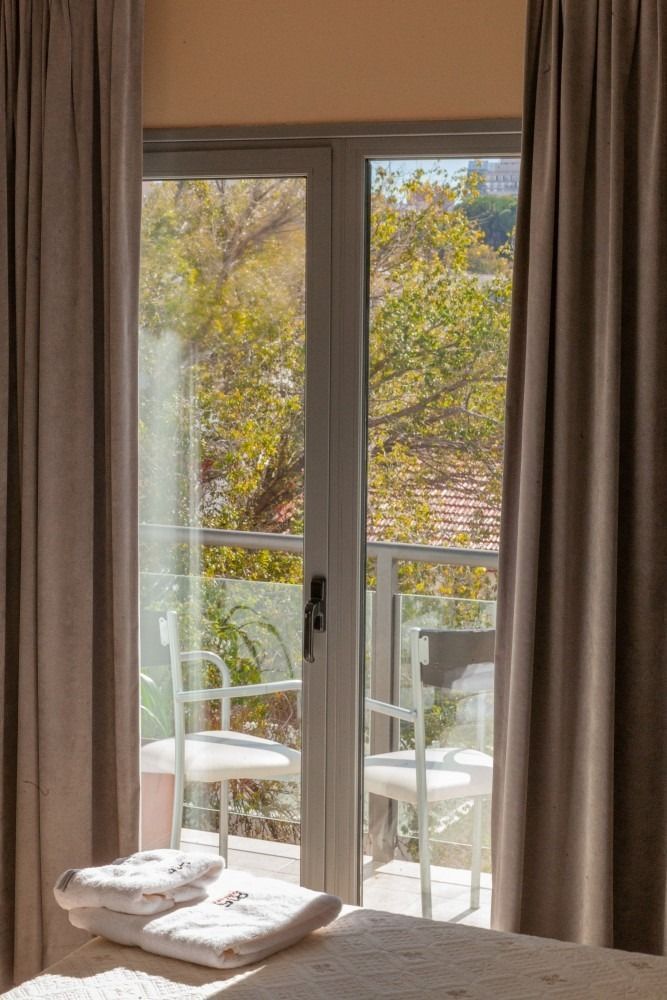 A view from inside a room through a glass door to a small balcony with two white chairs.