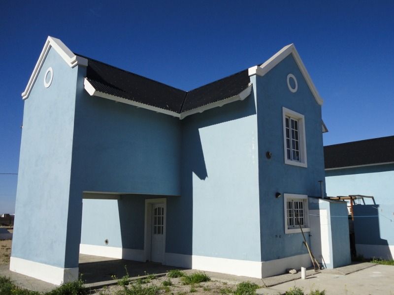 Blue house with white trim against a clear blue sky. It has an open carport and a black roof.