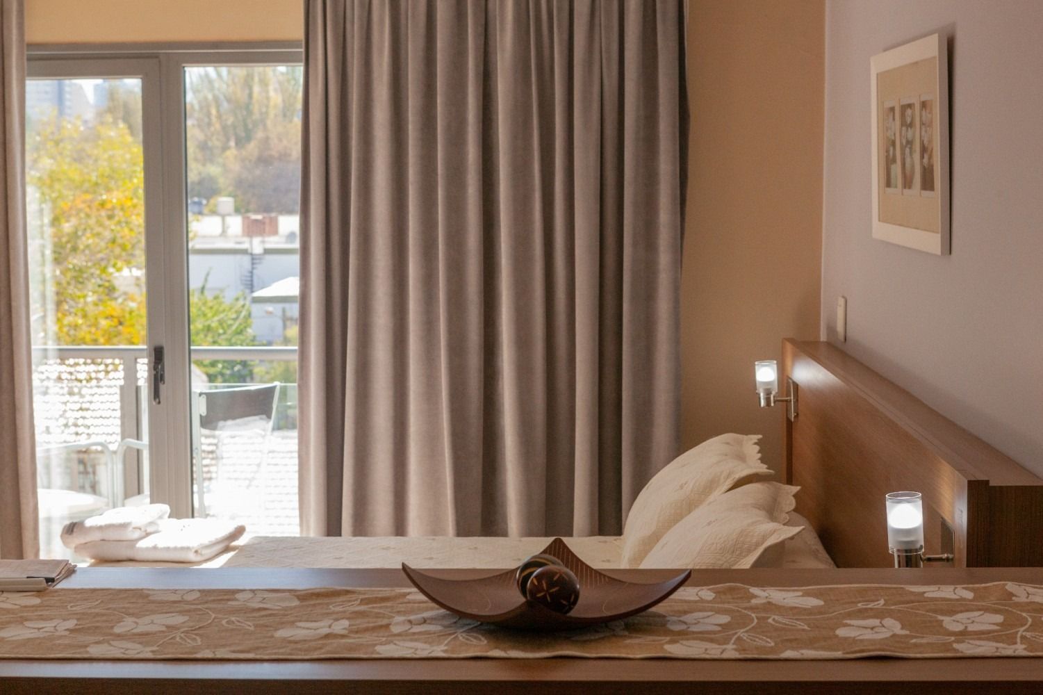 Bedroom with bed, balcony view, neutral tones, wood headboard, tan curtains, decorative tray.