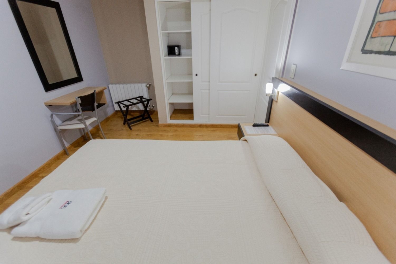 Hotel room with bed, wardrobe, desk, mirror, and luggage rack.