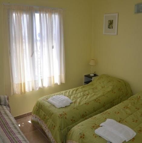 Bedroom with three twin beds; two green, one striped, white curtains, and soft lighting.