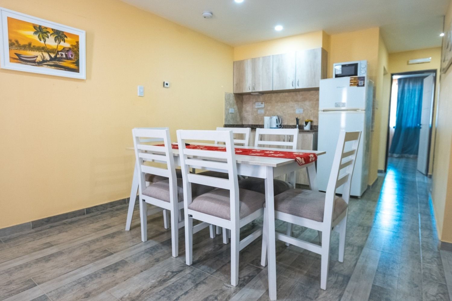 Dining area with a table and chairs, kitchen in the background, hardwood floor.