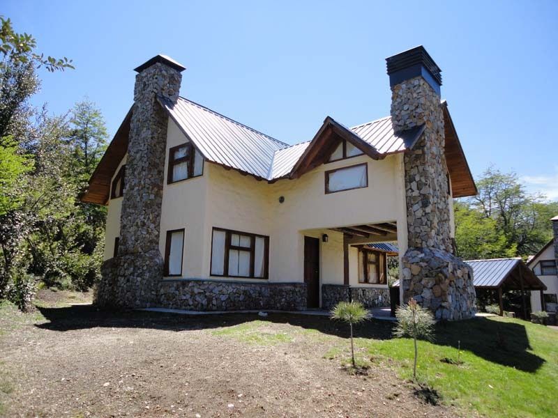 Two-story house with stone chimneys and a metal roof against a blue sky.