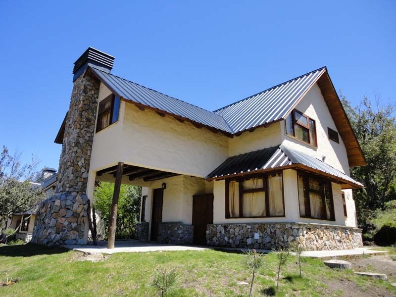 Beige two-story house with stone chimney and foundation; blue sky in background.