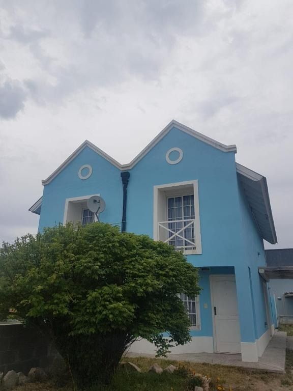 Light blue two-story house with white trim, under a cloudy sky. A bush is in front.