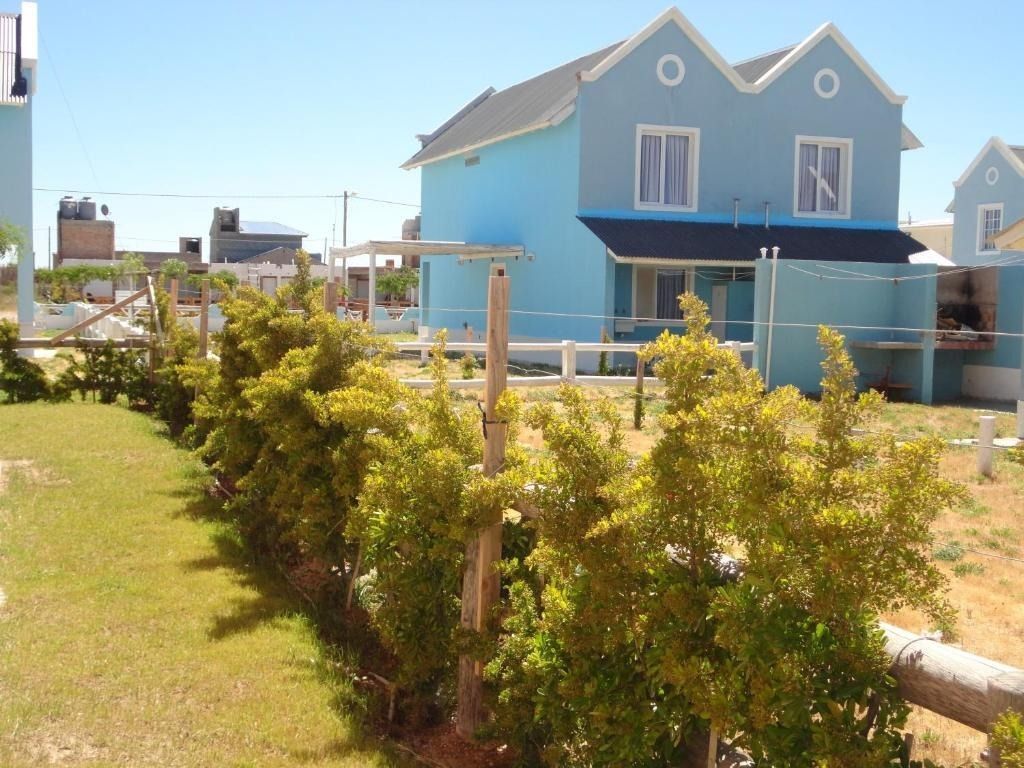 Blue house with white trim, a dark roof, and a hedge on a sunny day.