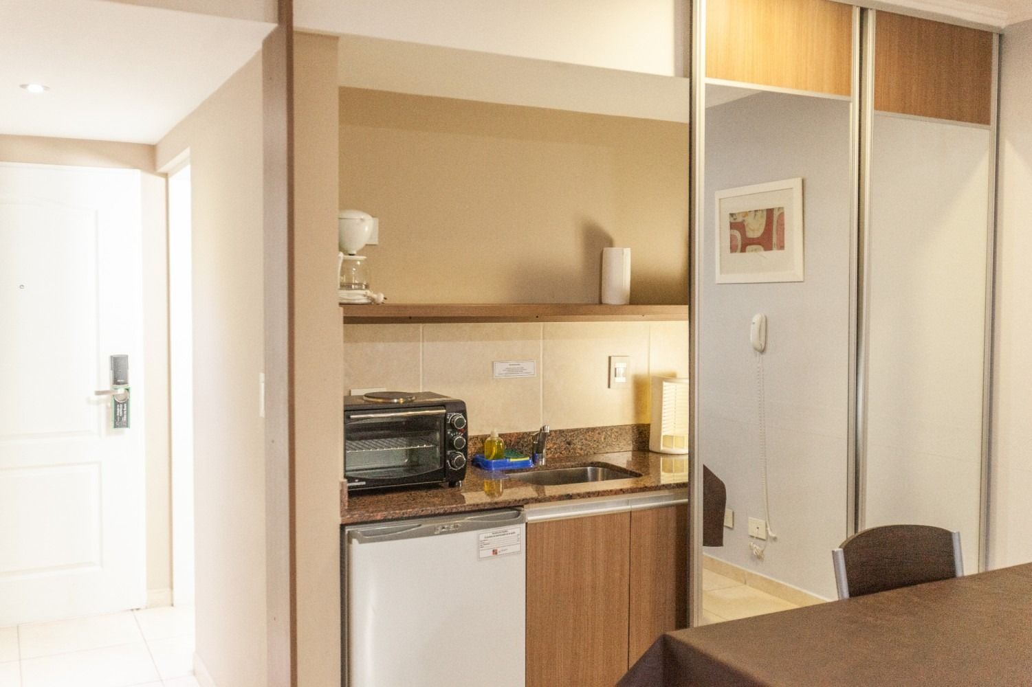 Small kitchenette with a microwave, sink, and mini-fridge in a room with a mirrored closet.