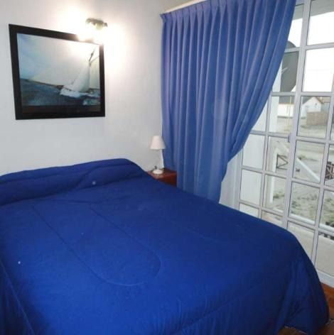 Bedroom with a blue bedspread, curtains, and artwork; a window is visible.