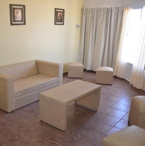 Beige living room with a sofa, ottomans, coffee table, and window with curtains.
