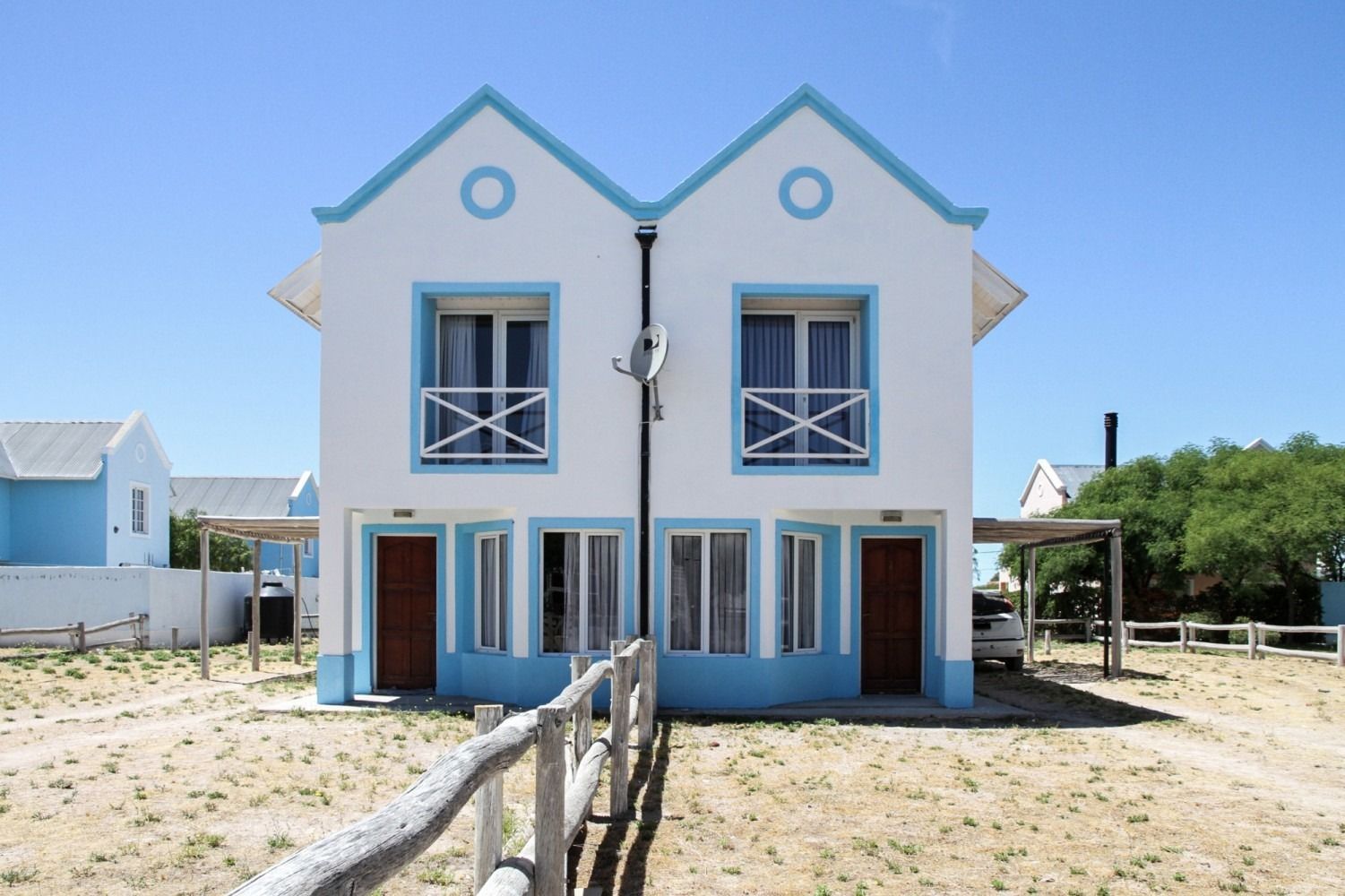 Two-story white and blue duplex building with wooden fence on a sunny day.