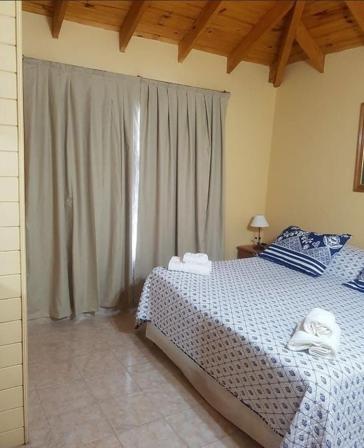 Bedroom with a bed, beige curtains, and wood ceiling. The bed has blue patterned bedding and white towels.