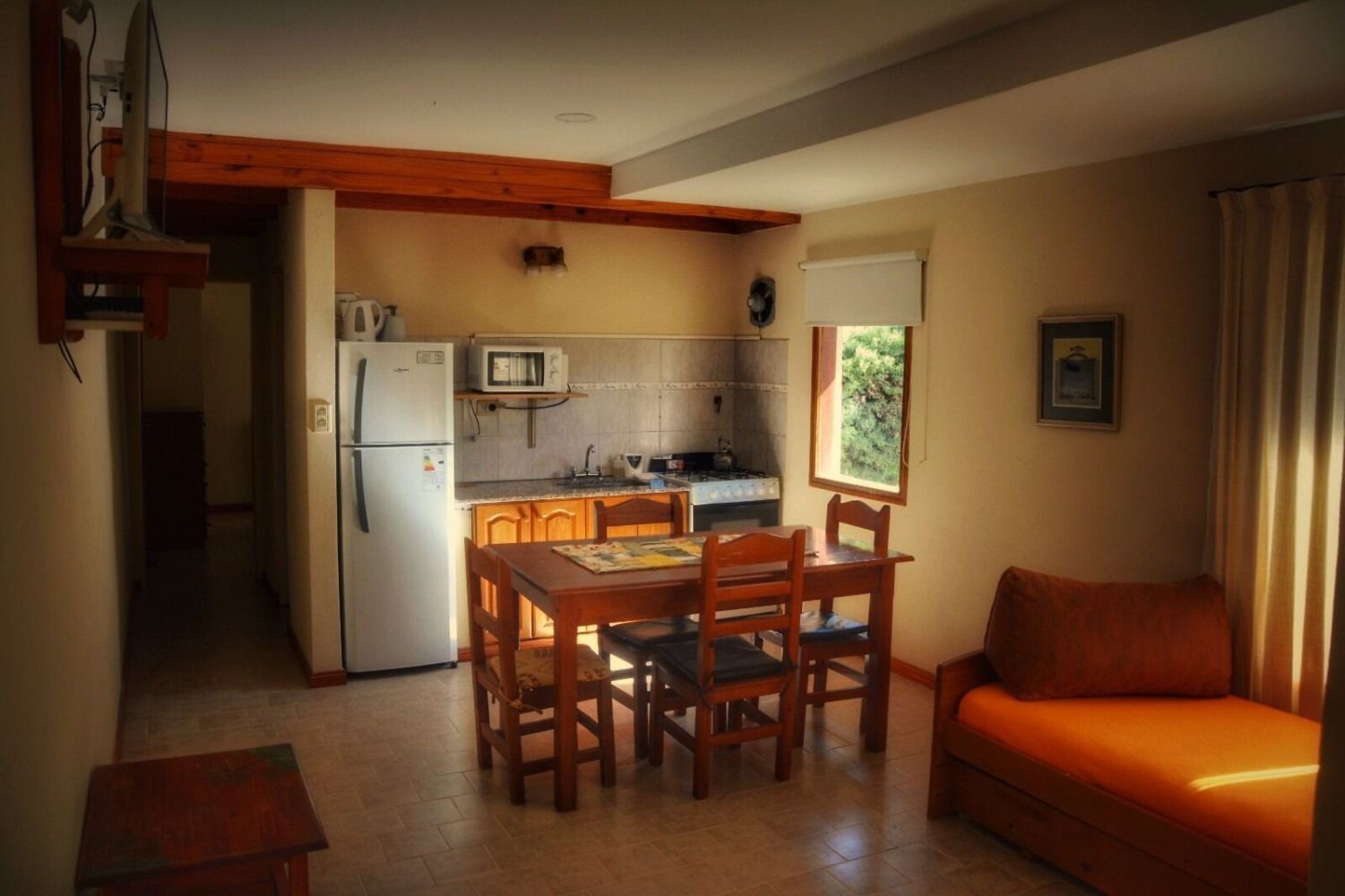 Small kitchen and dining area with refrigerator, table, and orange couch.