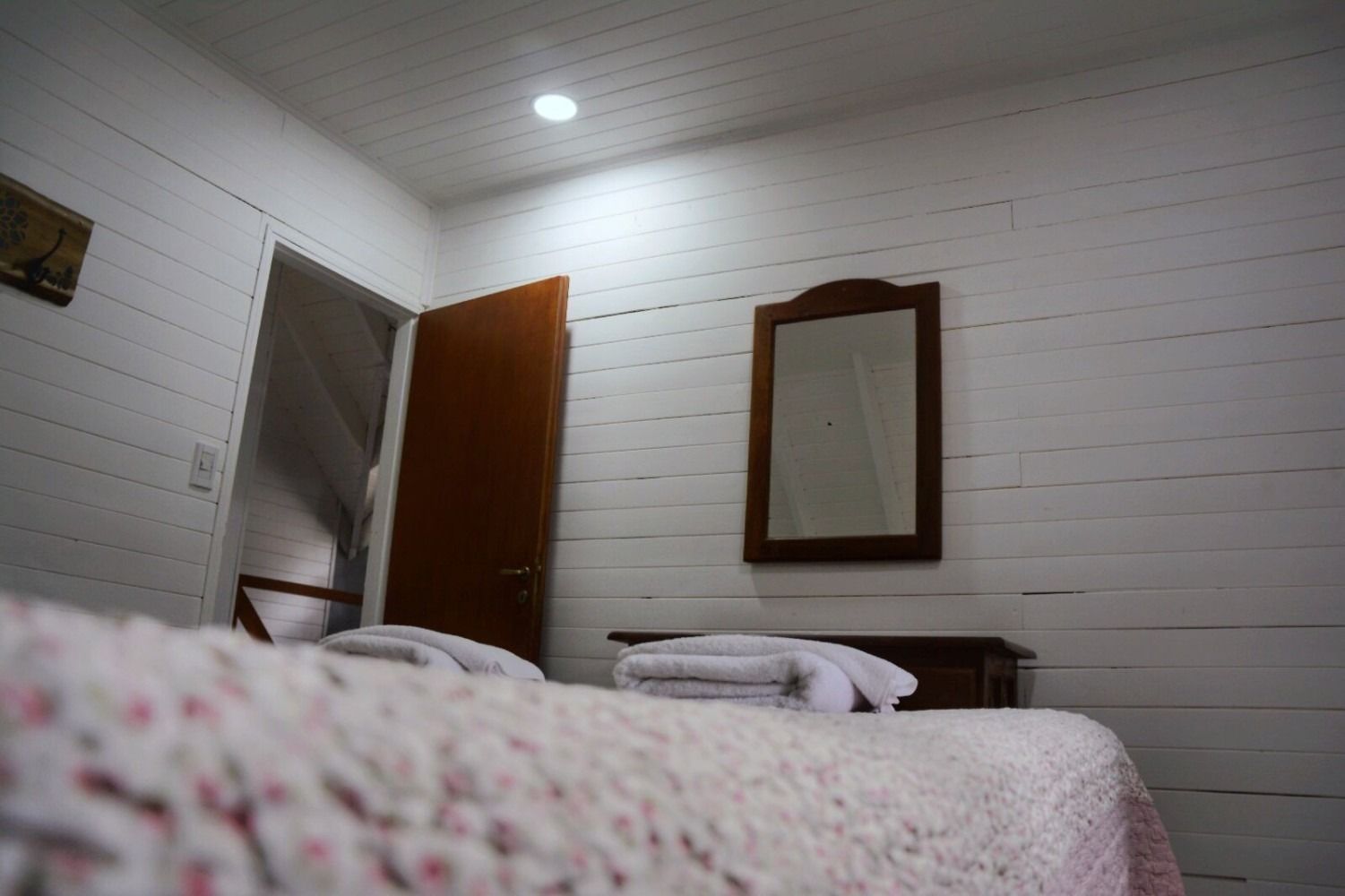 Bedroom interior with white paneled walls, bed, mirror, and doorway.