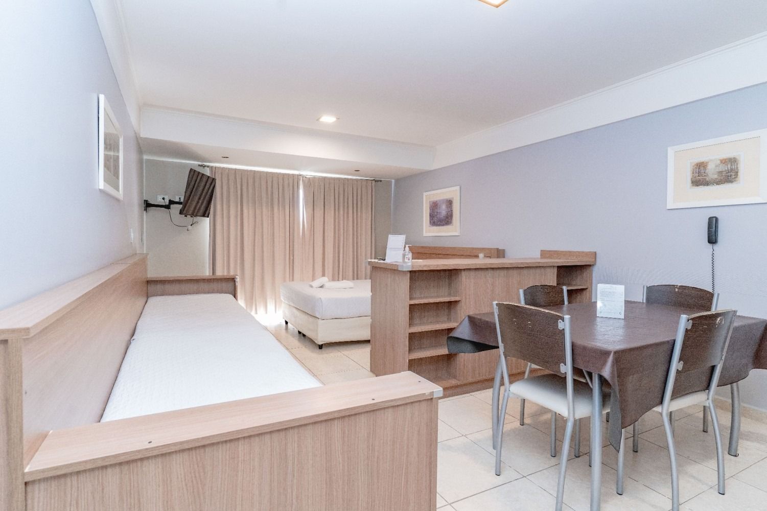 Small apartment with dining area, sofa-bed, bed, TV, light wood furniture, and gray walls.