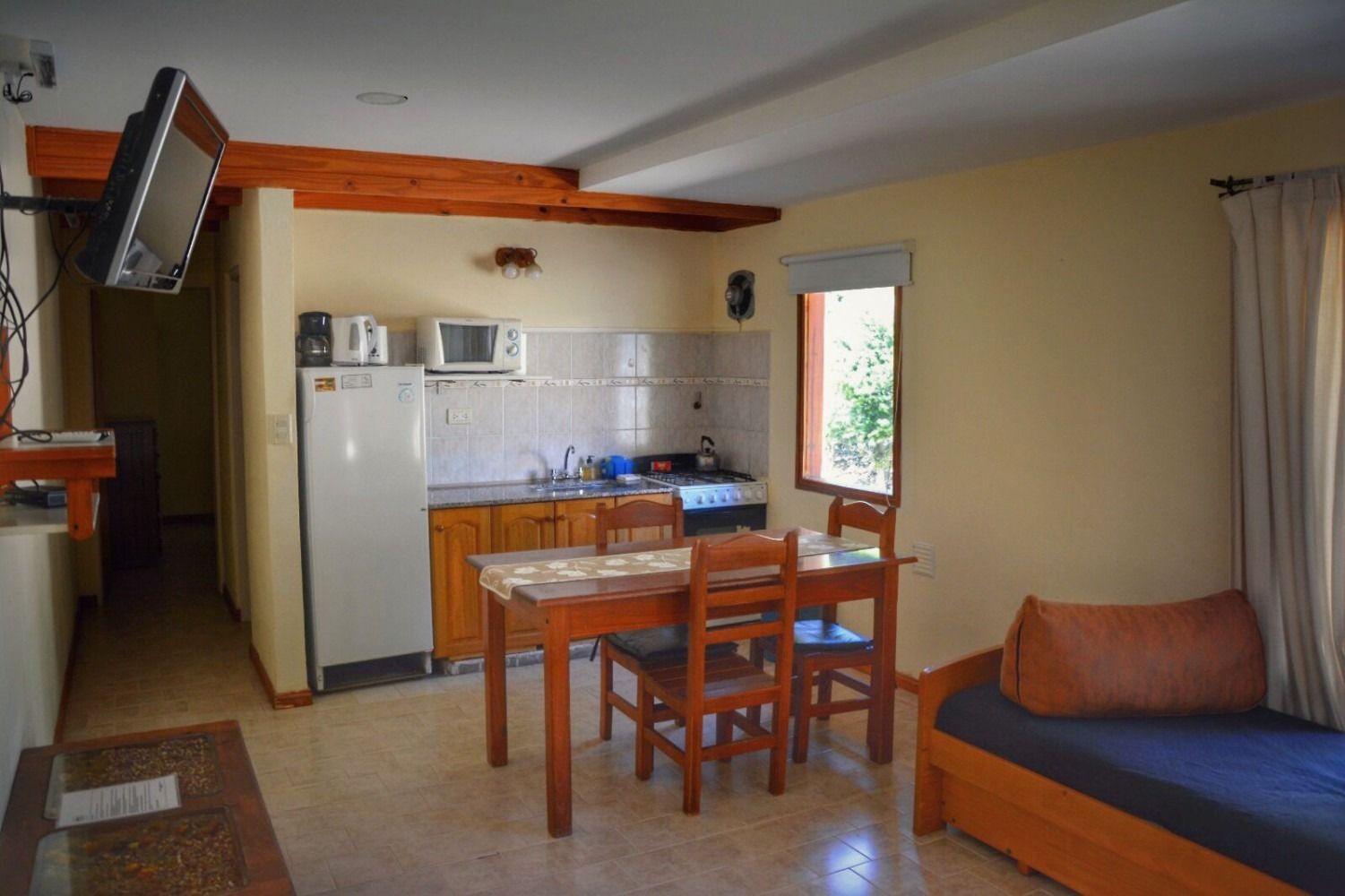 Small studio apartment with kitchenette, dining table, and sofa. Natural light streams in from a window.
