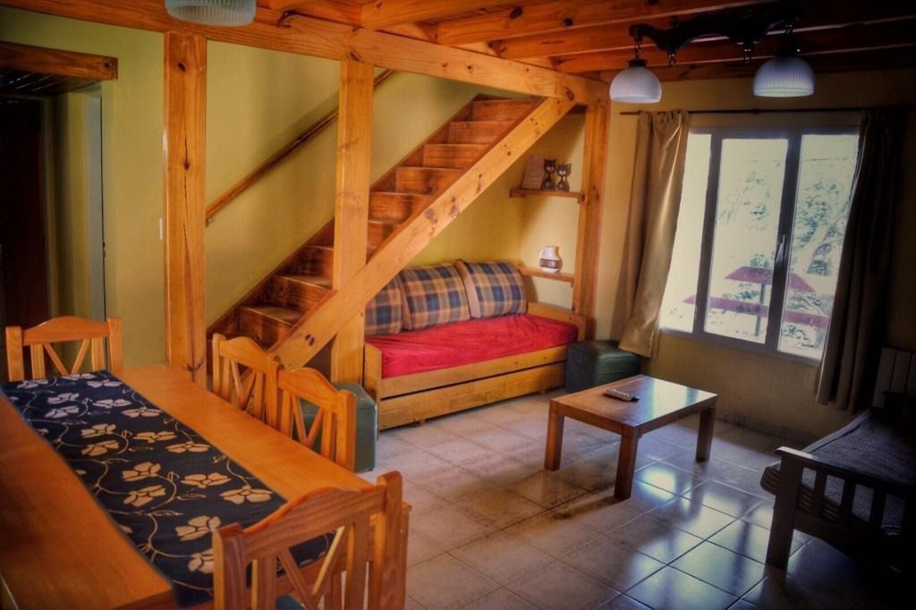 Wooden-beamed living area with staircase, dining table, sofa, and window with light coming in.
