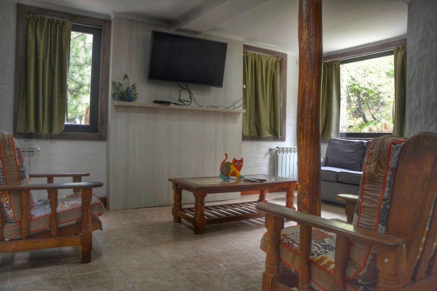 Living room with wooden furniture, TV, and windows with green curtains.