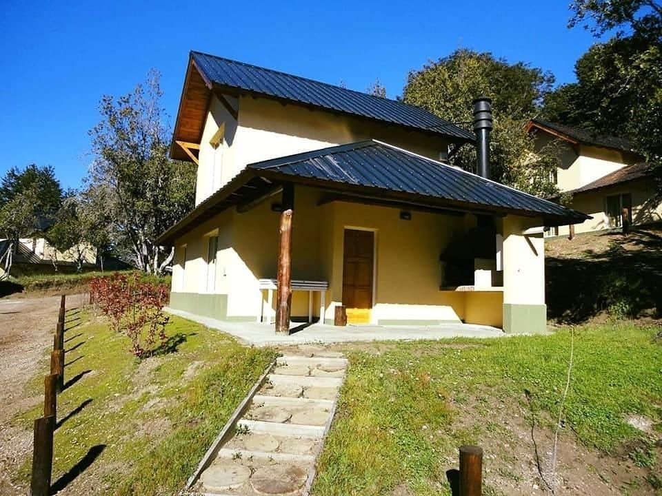 Cottage with a black metal roof, on a grassy hillside, steps leading up. Another cottage in the distance. Blue sky.