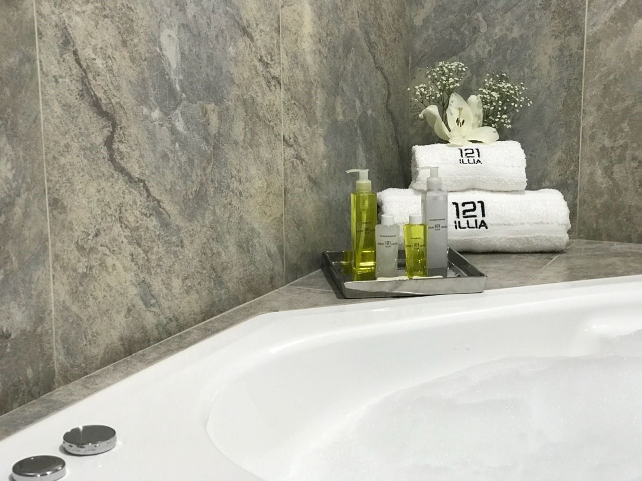 A luxury bathroom with a white tub, towels, toiletries, and marble-like wall.