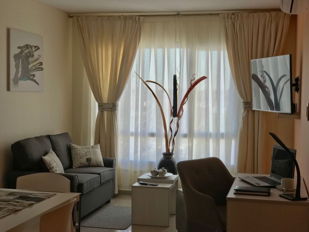 Cozy living space with a grey sofa, desk, and large window with sheer curtains.