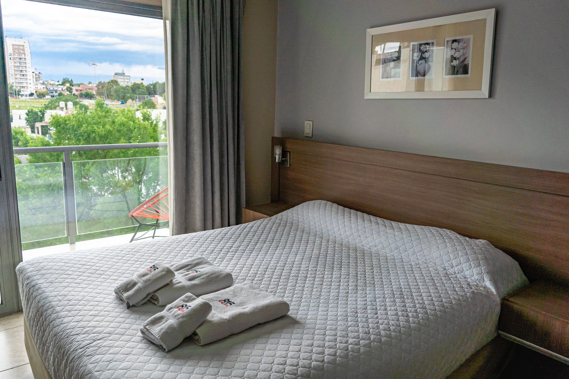 Bedroom with a bed, open balcony, framed photos on the wall, and towels on the bed.