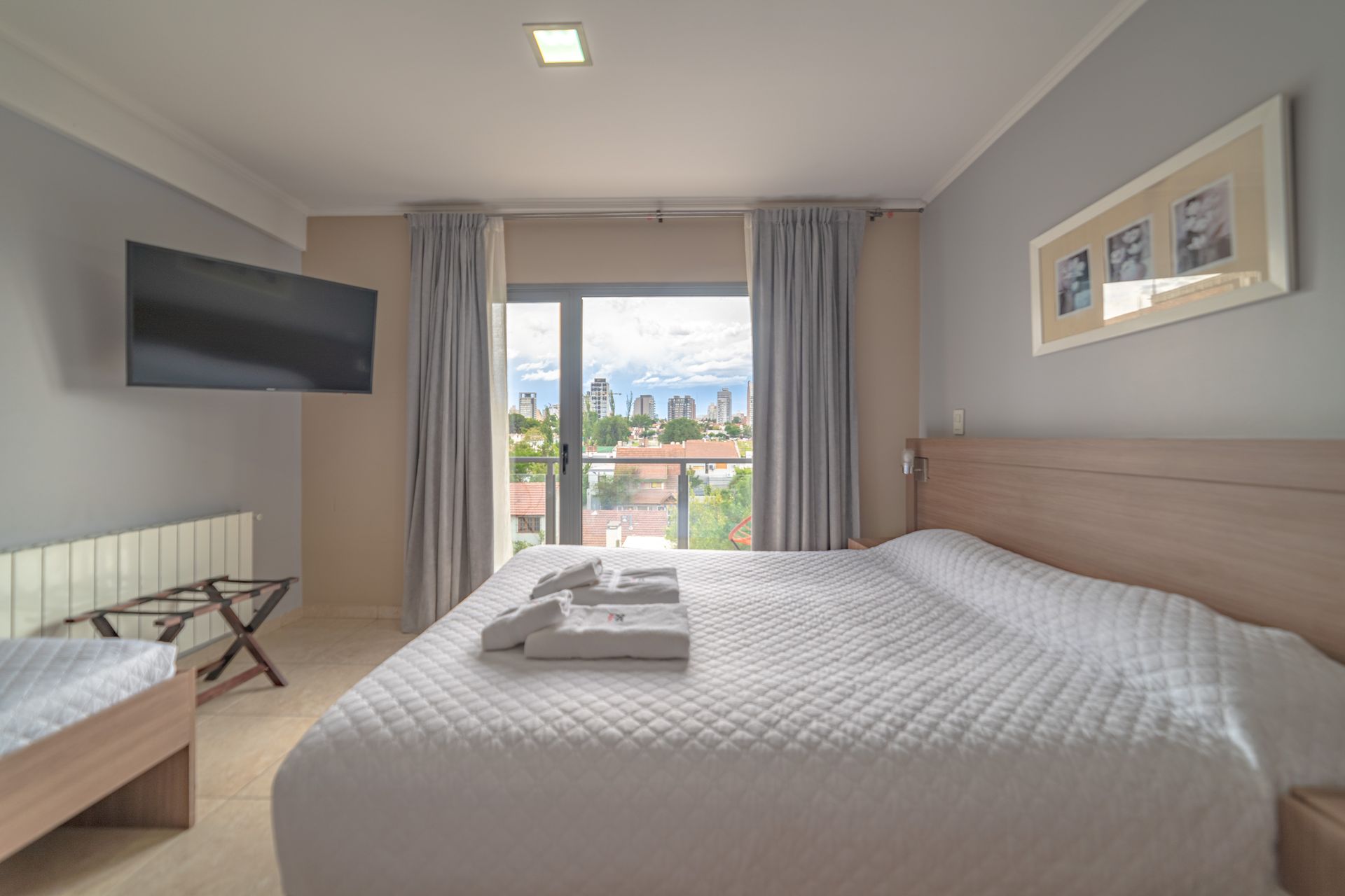 Bedroom with a large bed, TV, and balcony view of a city skyline.