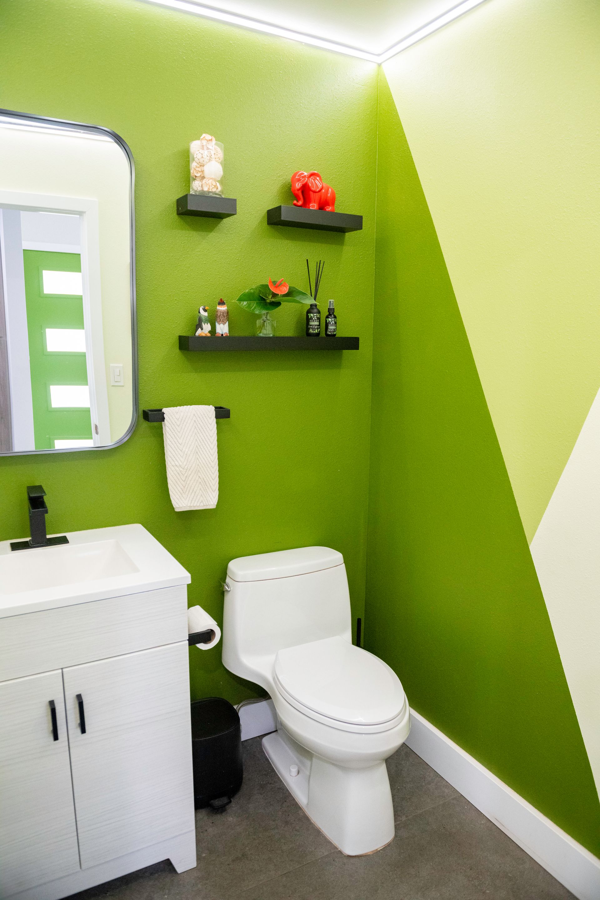 A bathroom with green walls , a toilet , sink and mirror.