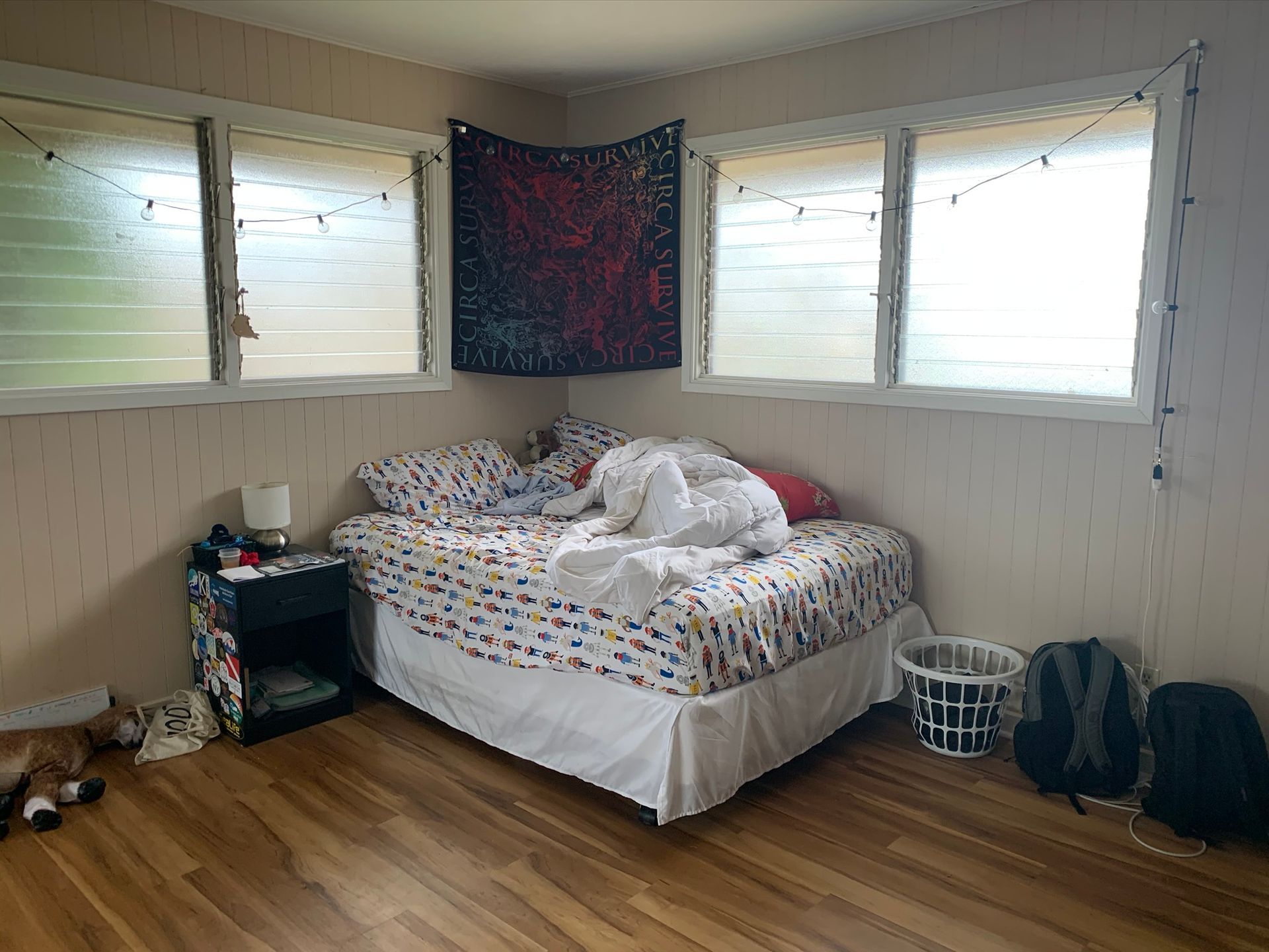 A bedroom with a bed , nightstand , and two windows.