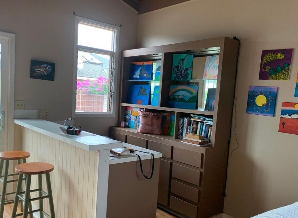 A room with a bar and a bookshelf with paintings on the wall.