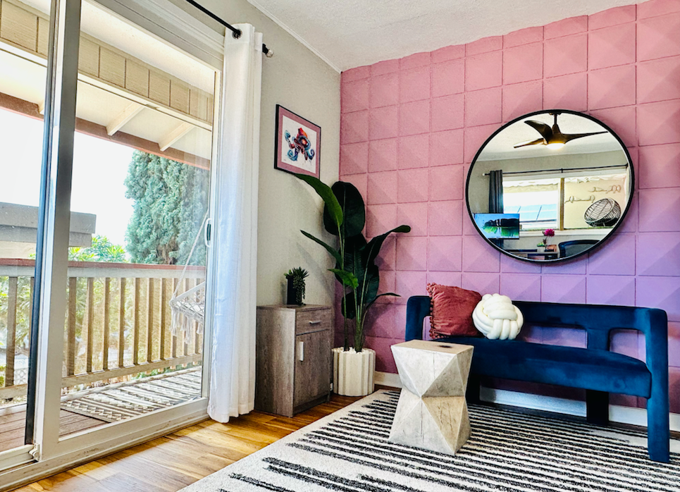 A living room with a pink wall , a blue couch , a round mirror and a sliding glass door.