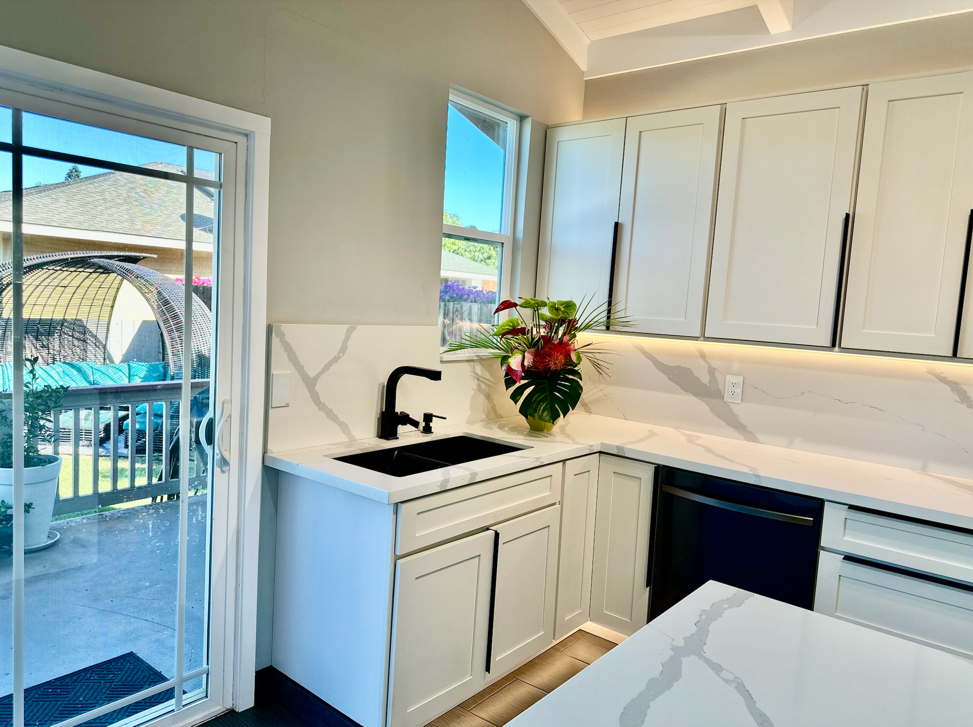 A kitchen with white cabinets , a sink , and a sliding glass door.