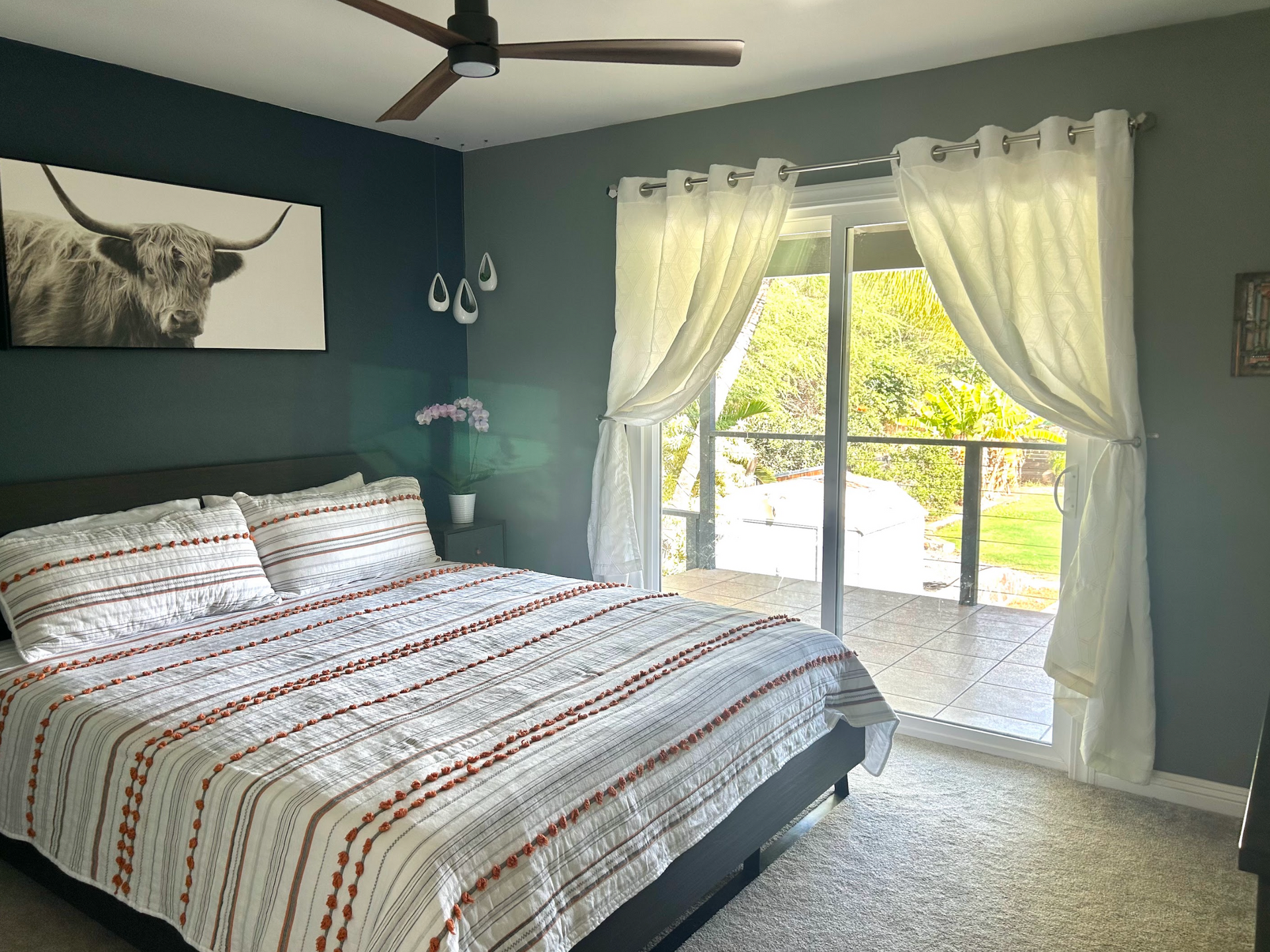 A bedroom with a king size bed , a ceiling fan , and a sliding glass door.