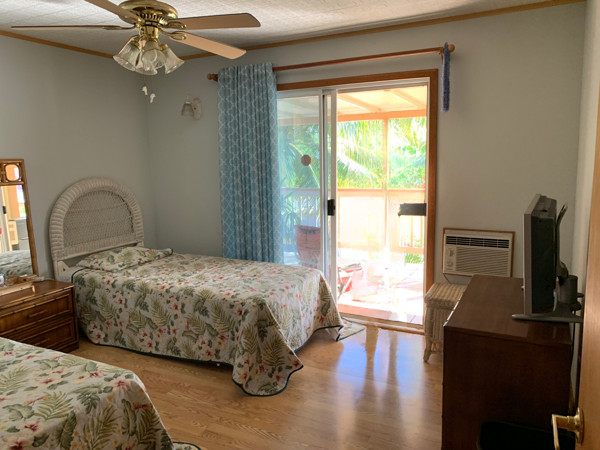 A bedroom with two beds , a ceiling fan , a television and a sliding glass door.