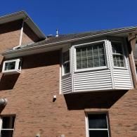 A two-story brick house exterior with a bay window on the second floor and a window air conditioning unit.