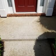 A concrete walkway leads up to a single step and a red front door framed by white trim.