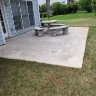 A light blue house exterior with a concrete patio featuring a stone table and matching bench on a green lawn.