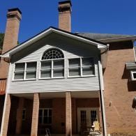 A rear view of a two-story brick house with a white-sided addition featuring arched windows above a covered patio.