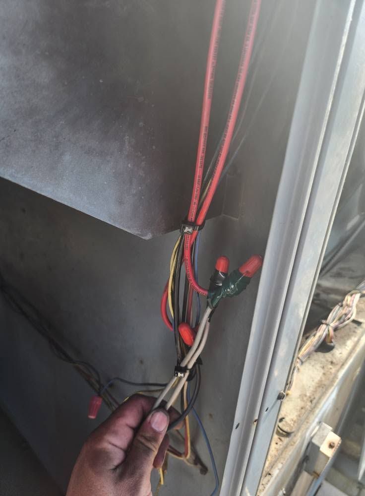 Hand holding bundled red, black, and white wires inside a gray electrical panel