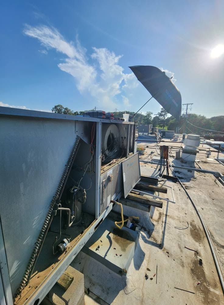 Rooftop HVAC unit with open panels and exposed wiring under a bright blue sky