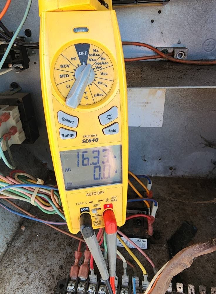 Yellow digital multimeter with probes attached, showing a reading in an electrical panel.