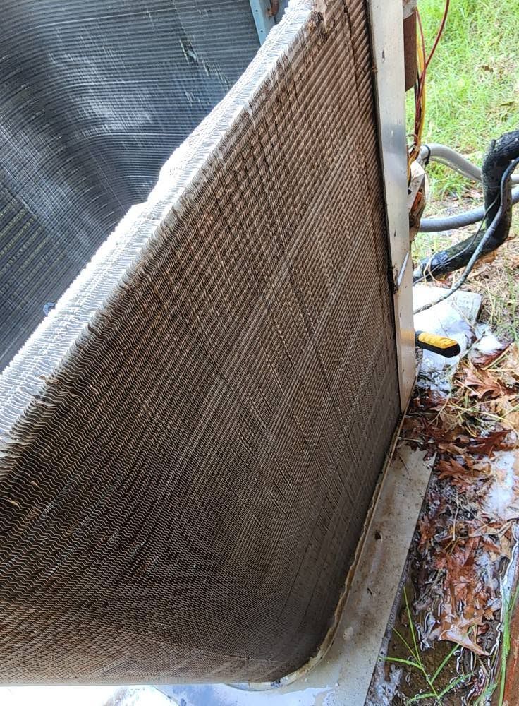 Outdoor HVAC condenser unit with a brown mesh cover beside a black tarp and garden hose