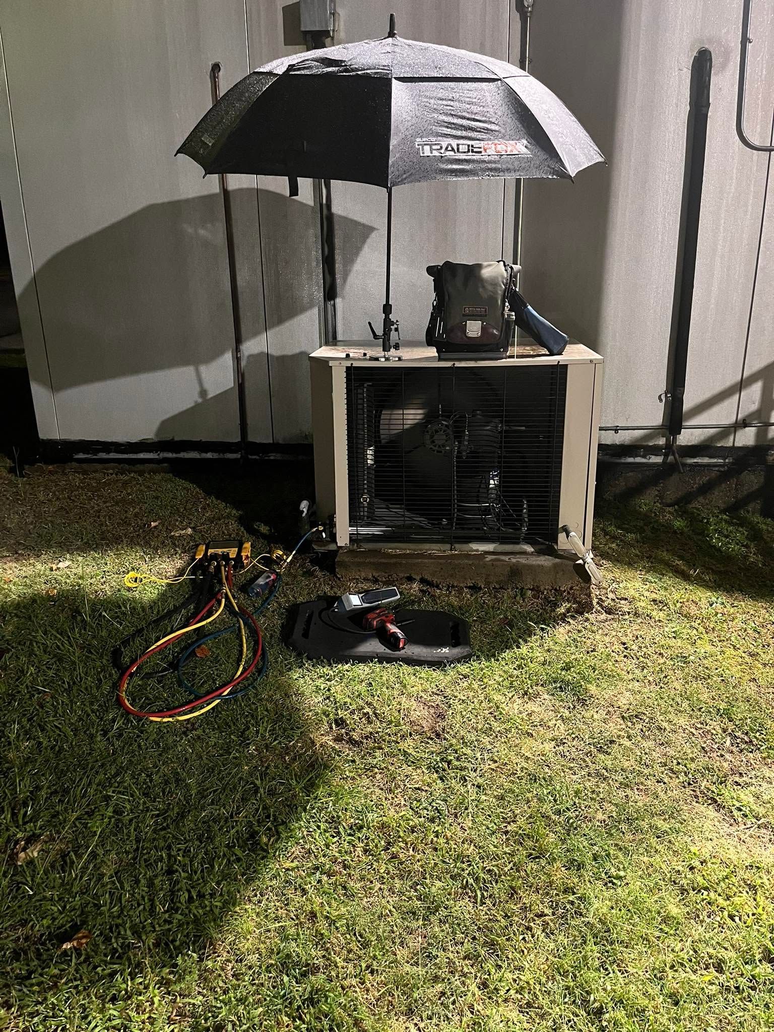 Umbrella shading a small outdoor device setup on grass beside a wall, with cables and a remote on the ground