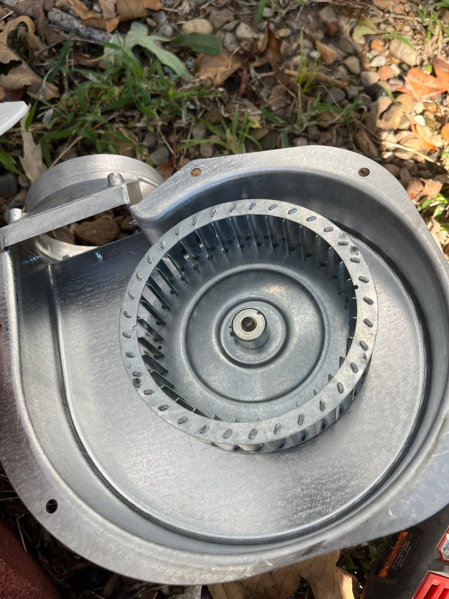 Close-up of a gray metal blower or fan housing with visible blades on the ground outdoors.