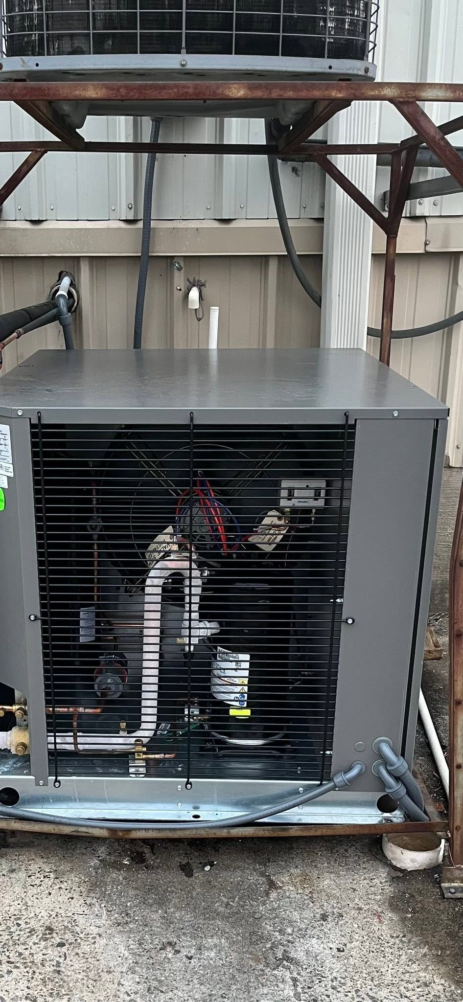Outdoor HVAC unit with exposed wiring and black front grille in a metal frame