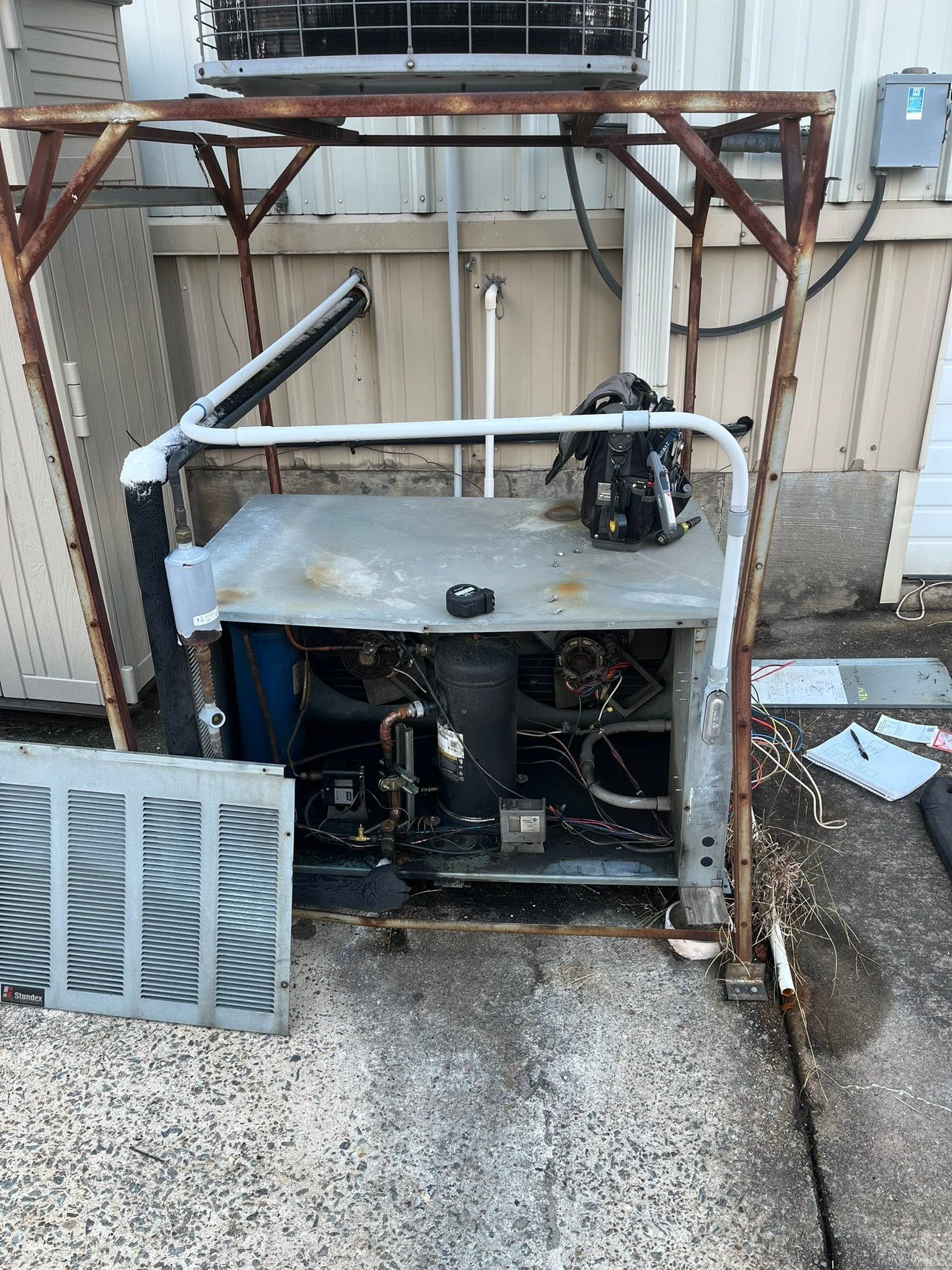 Damaged outdoor HVAC unit with exposed wiring and broken metal frame on a concrete surface