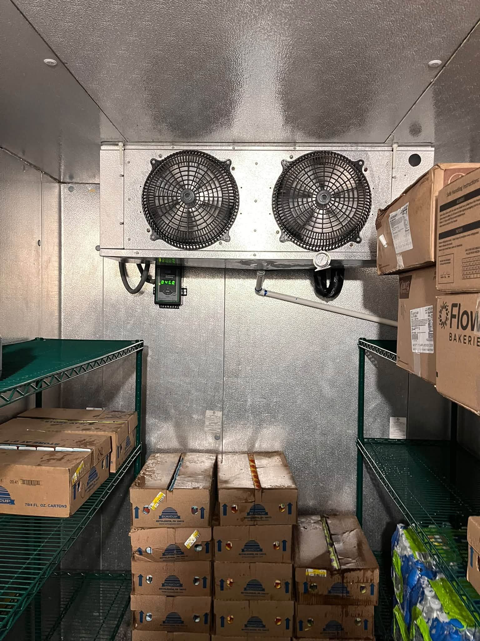 Walk-in cooler with two ceiling fans, cardboard boxes stacked on metal shelves and floor.