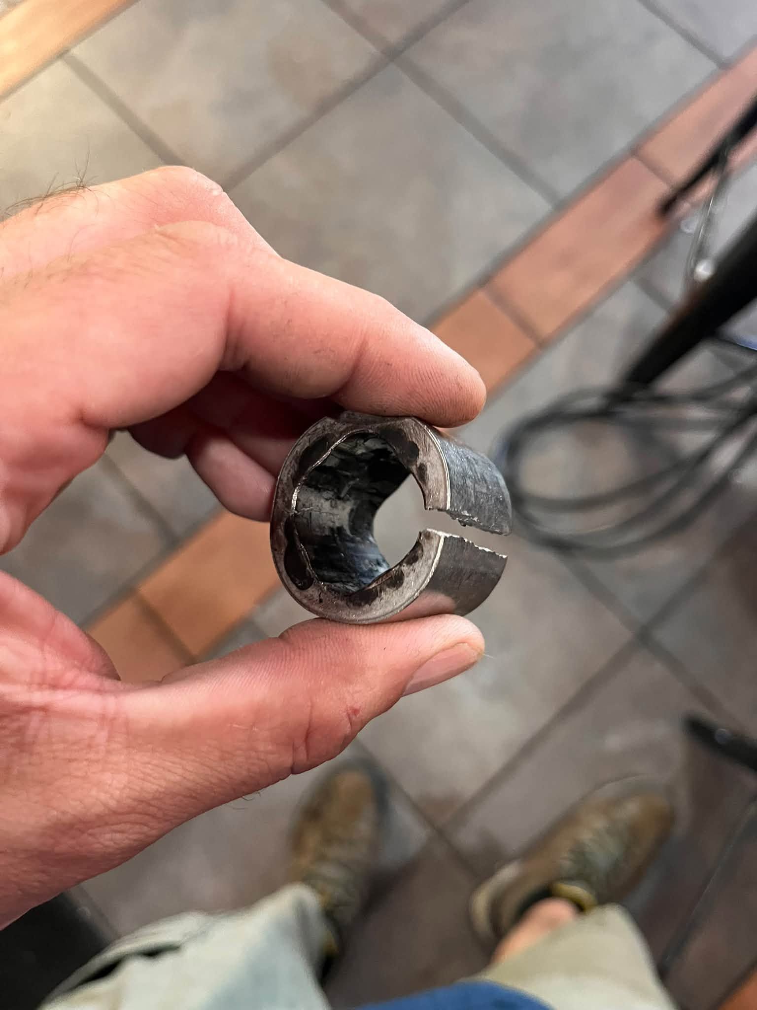 Hand holding a small broken metal socket or pipe fitting over a tiled floor.
