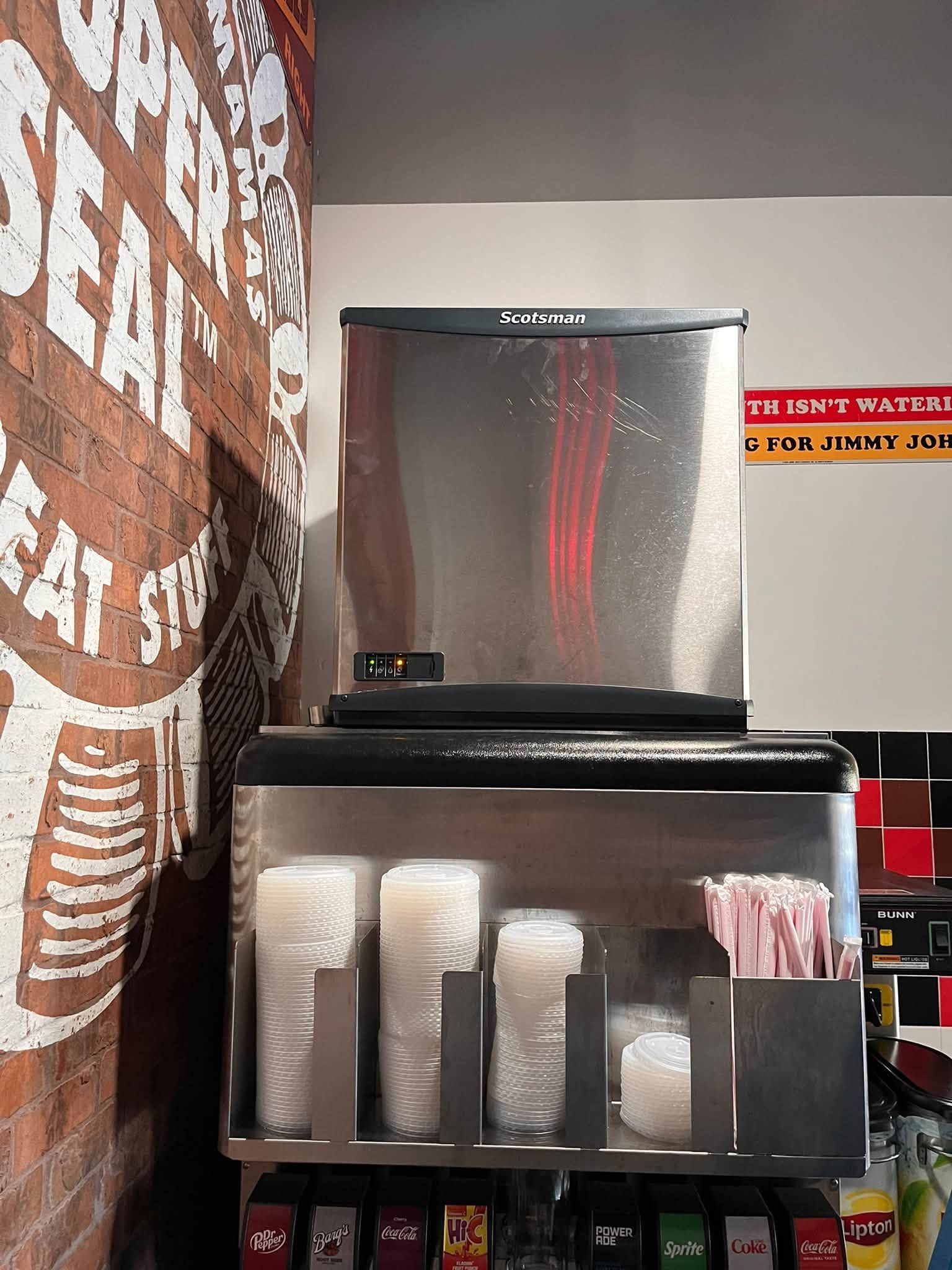 Display of clear plastic cups and containers on a black shelf in a store aisle.